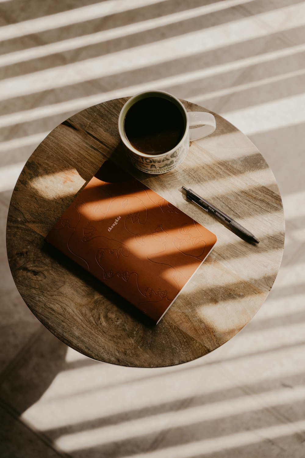 A notebook, pen and coffee on a small wooden table in morning light